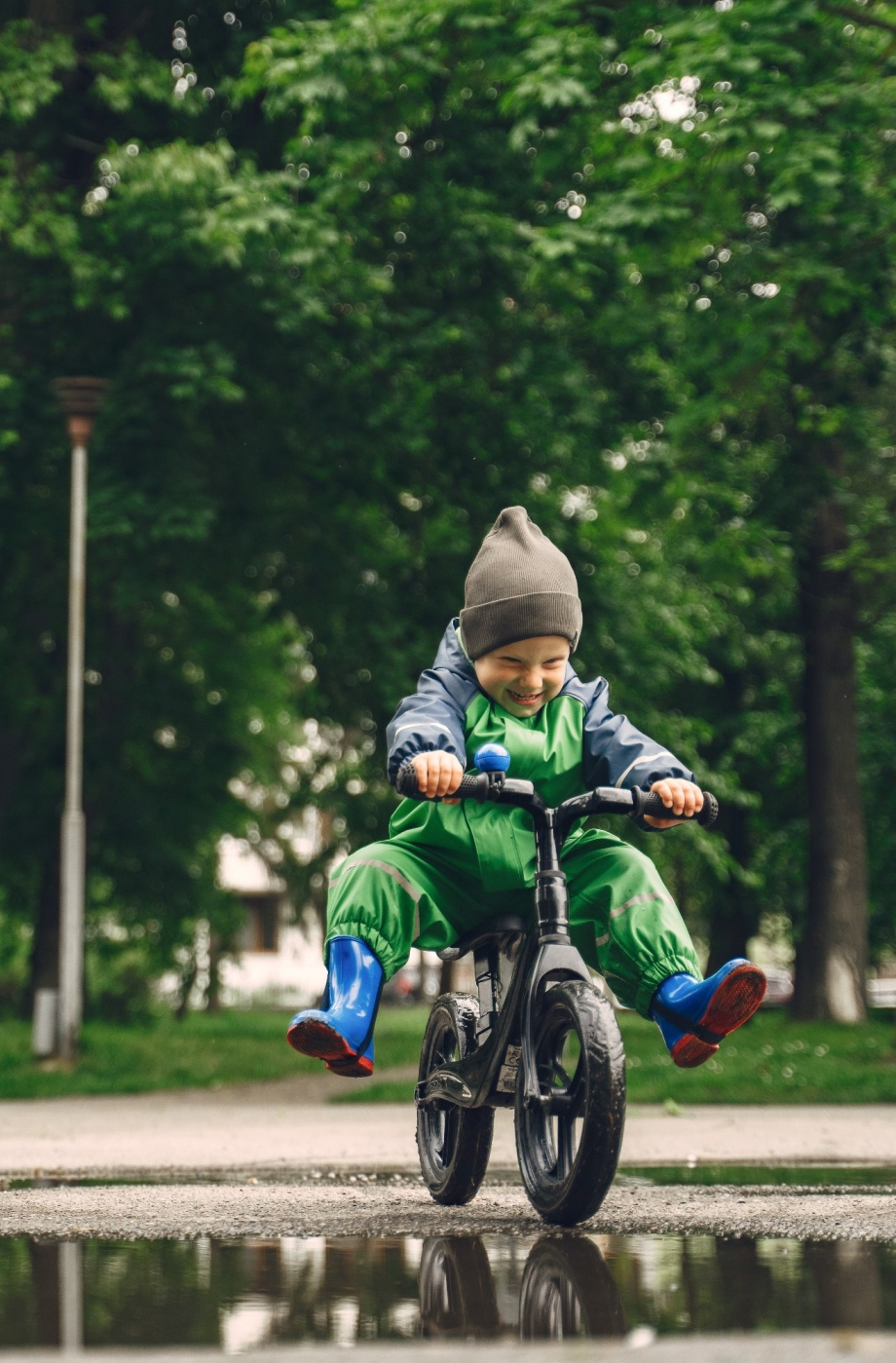 Funny kid in rain boots playing in a rain park